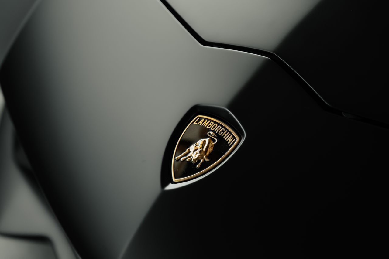 Detailed close-up photo of a Lamborghini logo on a sleek black car hood, symbolizing luxury and style.